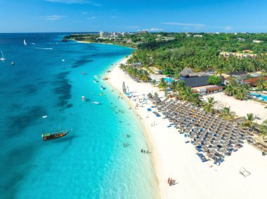 Palmiye ağaçları, şemsiyeler, yatlar, tekneler, mavi deniz, gün batımında bulutlu gökyüzü ile beyaz kumlu sahil manzarası. Kendwa, Zanzibar adasında yaz tatili. Tropik bir manzara. Temiz okyanus. Üst görünüm
