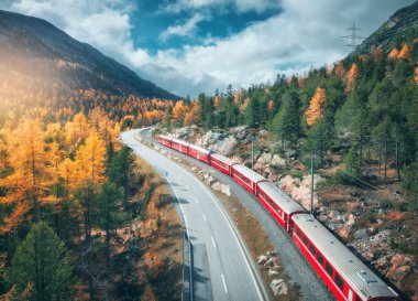 Alp dağlarındaki modern kırmızı trenin havadan görünüşü, yol, turuncu orman, sonbaharda günbatımında bulutlu gökyüzü. Bernina Express, İsviçre. Alplerdeki trenin en iyi insansız hava aracı görüntüsü, sonbaharda demiryolunu saran...