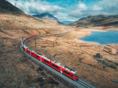 Sonbaharda günbatımında bulutlarla birlikte dağ gölü ve gökyüzü yakınlarındaki modern kırmızı trenin hava manzarası. Bernina Express, İsviçre. Alplerdeki hız treni manzarası, dolambaçlı demiryolu, sonbaharda turuncu tepeler..