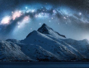 Samanyolu kışın yıldızlı gecesinde güzel karlı dağın üzerinde. Lofoten Adaları, Norveç. Parlayan Samanyolu kemeri, yıldızlar, karlı kayalar ve fiyortlu gökyüzü ile renkli bir manzara. Boşluk. Doğa