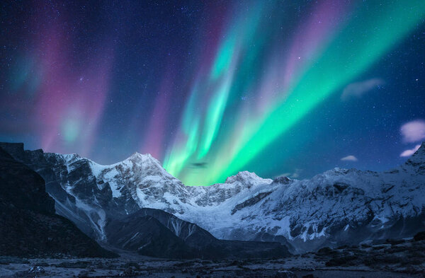 Северное сияние над снежными горами ночью в Лофотене, Норвегия. Aurora borealis над покрытыми снегом скалами. Зимний пейзаж с полярными огнями, горная вершина. Прекрасное звездное небо с сиянием