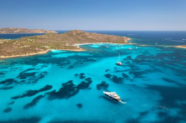 Lüks yatların ve mavi denizdeki teknelerin havadan görünüşü yaz güneşli günlerinde güzel bir ada. Kumsal, kayalık deniz kıyısı, Sardinya, İtalya 'da şeffaf turkuaz su. Üst dron görüntüsü. Deniz kenarında. Seyahat