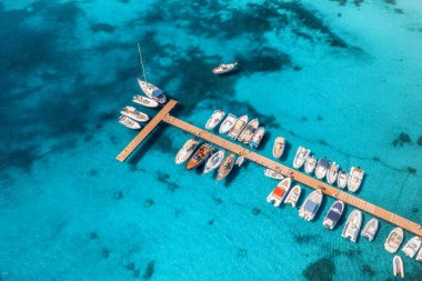 Aerial view of boats and luxure yachts in dock at sunset in summer in Sardinia, Italy. Colorful landscape with sailboats and motorboats in sea bay, jatty, clear blue sea. Top view of harbor. Travel