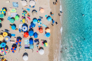 Kumlu sahildeki renkli şemsiyeler, güneşli yaz günlerinde mavi denizde yüzen insanlar. Sardunya, İtalya. Berrak gök mavisi suyu olan tropik bir yer. Seyahat ve tatil. Deniz kenarının üst görünümü