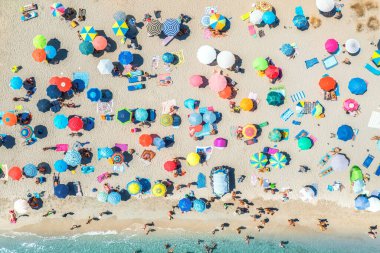Kumlu sahildeki renkli şemsiyeler, güneşli yaz günlerinde mavi denizde yüzen insanlar. Sardunya, İtalya. Berrak gök mavisi suyu olan tropik bir yer. Seyahat ve tatil. Deniz kenarının üst görünümü