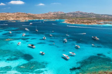 Lüks yatların ve mavi denizdeki teknelerin havadan görünüşü güzel bir ada, yaz güneşli bir günde dağ. Kumsal, kayalık deniz kıyısı, İtalya, Sardinya 'da masmavi şeffaf su. Üst dron görüntüsü. Deniz Burnu