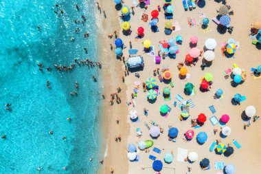 Kumlu sahildeki renkli şemsiyeler, güneşli yaz günlerinde mavi denizde yüzen insanlar. Sardunya, İtalya. Berrak gök mavisi suyu olan tropik bir yer. Seyahat ve tatil. Deniz kenarının üst görünümü
