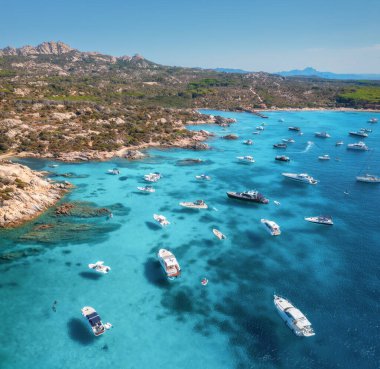 İtalya 'nın Sardunya adasındaki Maddalena takımadalarının güneşli yaz gününde kristal berraklığında turkuaz su içinde lüks yatları ve tekneleriyle nefes kesici manzarası. Mavi denizdeki teknelerin insansız hava aracı görüntüsü