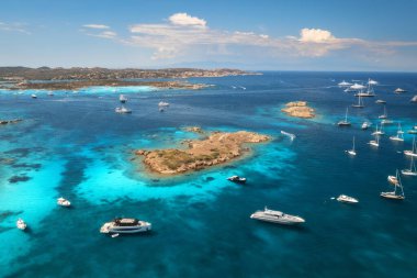 İtalya 'nın Sardunya adasındaki Maddalena takımadalarının güneşli yaz gününde kristal berraklığında turkuaz su içinde lüks yatları ve tekneleriyle nefes kesici manzarası. Mavi denizdeki teknelerin insansız hava aracı görüntüsü