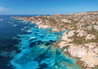 Sardunya adasındaki La Maddalena takımadasının kayalık kıyı şeridi boyunca demirlemiş lüks yatları çekerken nefes kesici hava manzarası canlı turkuaz suları ortaya çıkarıyor. Teknelerin ve mavi denizin en üst manzarası