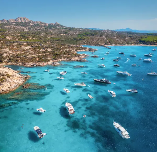İtalya 'nın Sardunya adasındaki Maddalena takımadalarının güneşli yaz gününde kristal berraklığında turkuaz su içinde lüks yatları ve tekneleriyle nefes kesici manzarası. Mavi denizdeki teknelerin insansız hava aracı görüntüsü