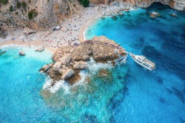 Güneşli yaz gününde insanlarla ve taşlarla dolu teknelerin ve kumlu plajların havadan görüntüsü. Yatların insansız hava aracı manzarası, kayalık deniz kıyıları. Akdeniz 'de. İtalya 'nın Sardunya adasında seyahat et. Tropikal manzara