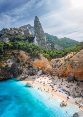 Kayaların ve dağların havadan görünüşü, mavi körfez, sahil, güneşli yaz günlerinde tekneler. Cala Goloritze, Sardunya Adası, İtalya. Uçurumların, taşların, yeşil ağaçların, gün batımında şeffaf masmavi suyun en üst drone görüntüsü