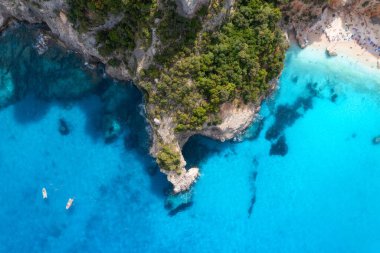 Güneşli yaz gününde şeffaf gök mavisi sulardaki teknelerin en iyi drone görüntüsü. Açık mavi deniz koyundaki teknelerin, kayaların ve yeşil ormanın havadan görüntüsü. Sardunya, İtalya 'ya seyahat. Tropik deniz manzarası. Doğa. Deniz Koyu