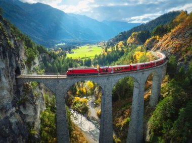 Alp dağlarındaki Landwasser viyadük üzerindeki modern kırmızı trenin havadan görünüşü, sonbaharda günbatımında renkli orman. Bernina Express, İsviçre. Alplerdeki tren manzarası, demiryolu, sonbaharda yeşil ağaçlar