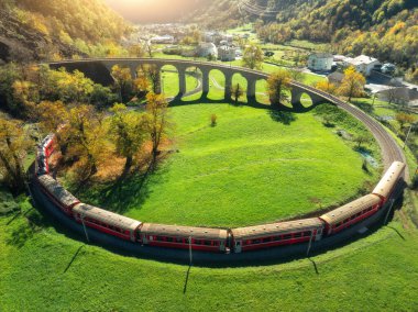 Sonbaharda gün batımında Kreisviadukt 'taki Alp Dağları' ndaki kırmızı trenin hava manzarası. Bernina Express, İsviçre. Tren manzarası, demiryolu, yeşil çimenler, sonbaharda renkli ağaçlar. the Spiral viyadük