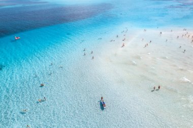 Yüzen insanlarla berrak mavi deniz manzarası. Kumsalın beyaz kumlu insansız hava aracı görüntüsü güneşli bir günde mavi şeffaf su. La Pelosa sahilinde yaz, Sardinya, İtalya. Tropikal manzara