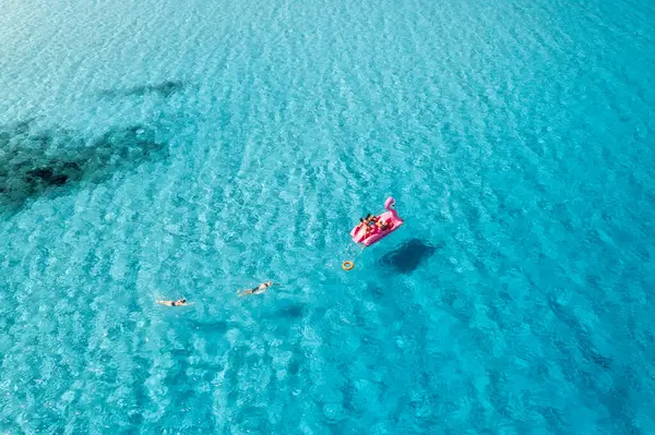 Yazın güneşli bir günde, berrak mavi suyun üzerinde insanların olduğu, şişme pembe flamingo manzarası. Aile fertlerinin teknedeki rahatlama manzarası, İtalya 'nın Sardinya Adası' ndaki masmavi deniz. Seyahat ve tatil