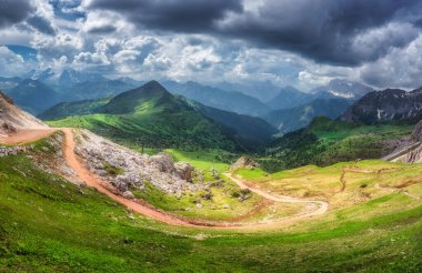 Renkli yeşil vadide dolambaçlı dağ yolu, yazları zıt ışık ve gölgelerle dolu dramatik bir gökyüzünün altındaki dağlık tepeler. Panoramik renkli manzara. Dolomitler, İtalya. Doğa
