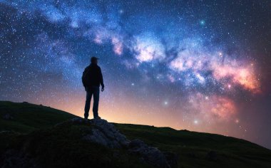 Parlayan Samanyolu ve yıldızlı gecede dağ yolunda bir adam. Tepede parlak yıldızlı bir adamın silueti. Galaksi. Samanyolu ile uzay manzarası. Gece manzarası. Seyahat geçmişi. Kavram