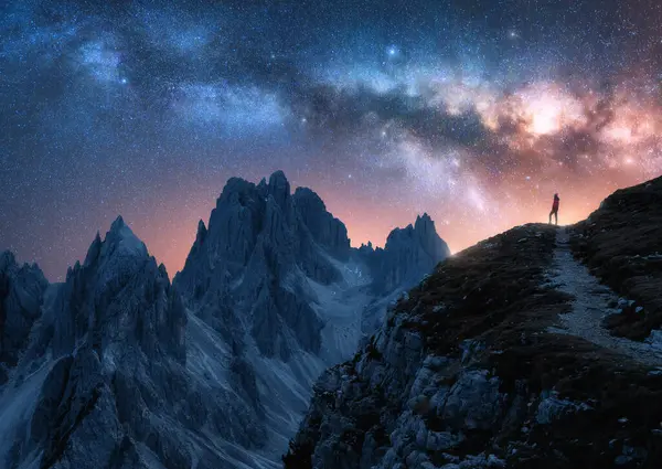 Parlayan Samanyolu ve yıldızlı gecede dağın zirvesinde bir kadın. Tre Cime, Dolomitler, İtalya. Galaksi. Bir kızın siluetiyle uzay manzarası, izler, kayalar, yıldızlı pembe gökyüzü. Samanyolu ve yürüyüşçü
