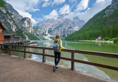Alp dağlarındaki Braies gölünde sırt çantalı genç bir kadın bulutlu mavi gökyüzü, berrak suda yansıması, günbatımında ahşap çit. Dolomitler, İtalya 'ya yaz seyahati. Göldeki kız. Yürüyüş