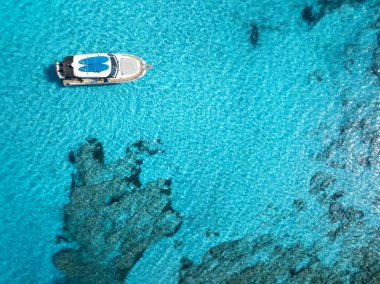 Kayalık deniz yatağının üzerinde, turkuaz turkuaz bir denizde yüzen beyaz bir yatın havadan görünüşü, Mallorca, Balearic Adaları, İspanya yakınlarındaki yaz tatili manzarası. Tekne ve gök mavisi suyun en üst hava aracı görüntüsü
