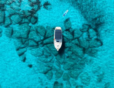 Beyaz yatın insansız hava aracı, sığ turkuaz denizde kayalık deniz yatağının üzerinde demirlemiş, yakınlarda yüzen raket, Mallorca, Balearic Adaları yakınlarında sakin bir yaz manzarası. Arkaplan