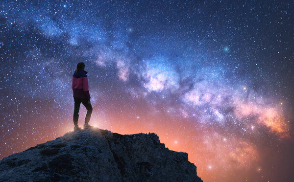 Светящийся Млечный Путь и женщина на вершине горы в звездную ночь. Доломиты, Италия. Галактика. Космический пейзаж с силуэтом девушки, скалы, небо с яркими звездами. Млечный Путь и турист. Nightscape