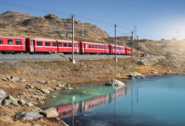 Günbatımında İsviçre 'de göl kenarındaki Bernina Express treni İsviçre Alpleri' nde berrak yansımalar, dağ siluetleri ve alp arazisinde huzurlu bir akşam ışığı altında. Kırmızı tren. Nakliye aracı. Tren istasyonu.