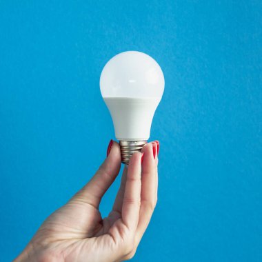 Bir kadının elindeki lamba. LED lamba tutan kadın parmakları. Bir fikrim var. Yeni fikir ya da ilham konsepti. Başlangıç konsepti. mavi arka plan. Kare resim.