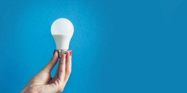 lamp in a woman's hand. female fingers holding LED lamp. idea. New idea or inspiration concept. Concept of startup. blue background. Banner for insertion into site. Horizontal image.