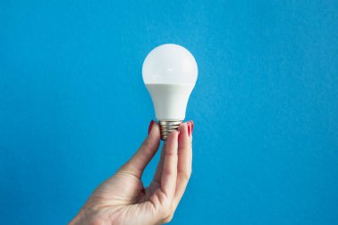 Bir kadının elindeki lamba. LED lamba tutan kadın parmakları. Bir fikrim var. Yeni fikir ya da ilham konsepti. Başlangıç konsepti. mavi arka plan. Yatay resim.