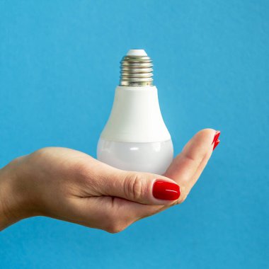 Bir kadının elindeki lamba. LED lamba tutan kadın parmakları. Bir fikrim var. Yeni fikir ya da ilham konsepti. Başlangıç konsepti. mavi arka plan. Kare resim.