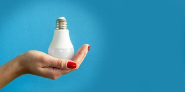 lamp in a woman's hand. female fingers holding LED lamp. idea. New idea or inspiration concept. Concept of startup. blue background. Banner for insertion into site. Horizontal image.
