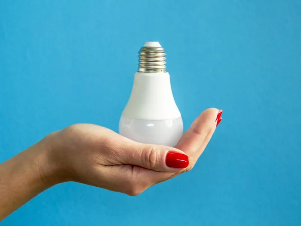 lamp in a woman\'s hand. female fingers holding LED lamp. idea. New idea or inspiration concept. Concept of startup. blue background. Horizontal image.