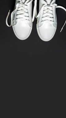 Siyah arka planda beyaz deri ayakkabılar. Beyaz bağcıklı beyaz spor ayakkabılar. Yeni ayakkabılar. Dikey resim.