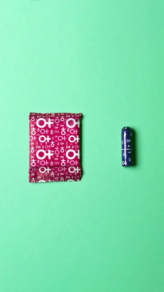 A sanitary napkin and a tampon lie on a green background. View from above. Gasket in red packaging. A tampon in a lilac package. Vertical image. Flatley