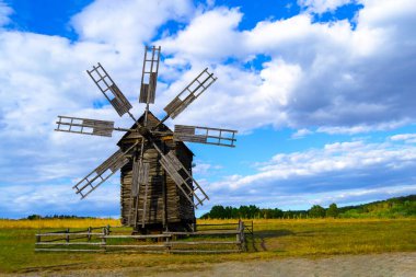 Photo of a windmill, taken in a picturesque rural landscape. A stationary windmill in windless weather. Horizontal image.