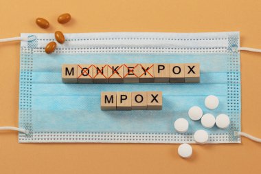 Maymun Çiçeği ve Mpox kelimeleri cerrahi maske takan tahta küplerle dizilmiştir. Harflerin üzeri kırmızı bir haçla çizilmiş. MPOX, maymun çiçeği virüsünün yeni adı..