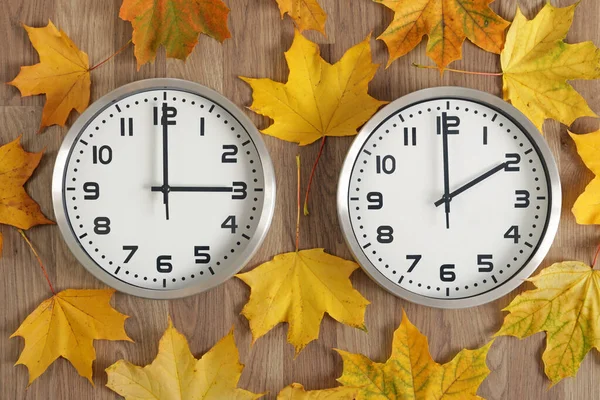 两个钟表 一个显示三点钟 另一个显示两点钟 秋天黄色的落叶散落在四周 时间的象征从夏天到冬天都在变化 手向后移动 — 图库照片