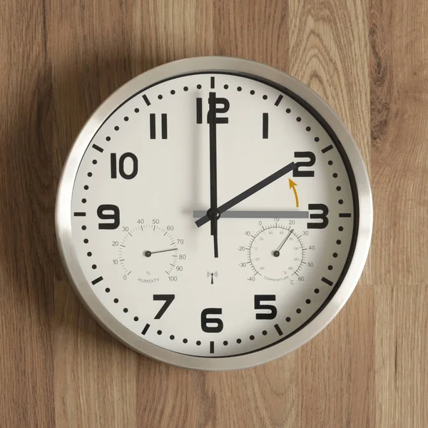 A clock, the gray hand points to three o\'clock, the black one to two o\'clock. The orange arrow indicates the direction of movement of the hands. Symbol of the time change. Standard time.