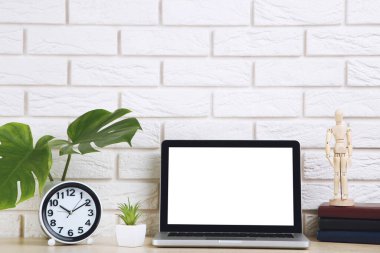 Yeşil yapraklı dizüstü bilgisayar, yuvarlak saat ve tuğla duvar zemininde tahta figür.