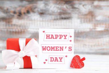 Card with text Happy Women's Day, gift and heart-shaped clothespin on wooden background