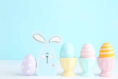 Colorful easter eggs in stands and wooden rabbit on blue background