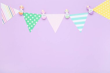 Easter concept. Paper flags and clothespins with rabbit faces on purple background
