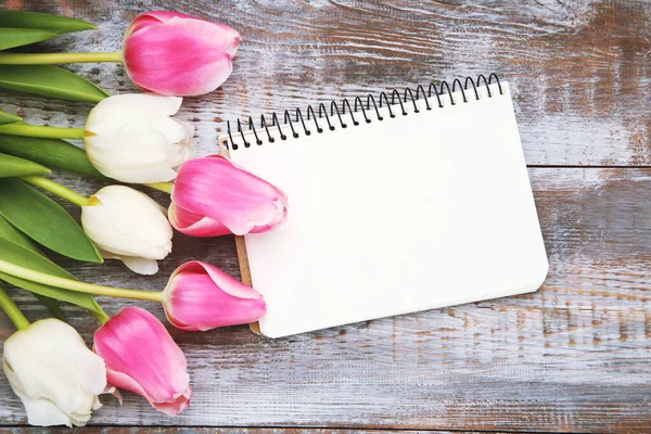 Bouquet flowers of tulips and notepad with space for text on wooden background