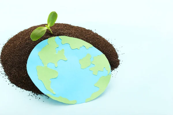 Earth day concept. Green sprout growing out from soil with paper planet