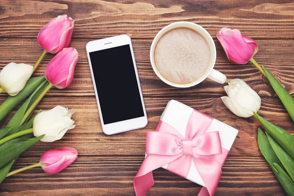 Tulpenblumen Geschenkbox Smartphone Und Kaffeetasse Auf Braunem Holzhintergrund lizenzfreie Stockbilder