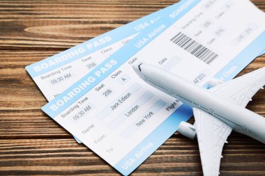 Kahverengi ahşap arka planda uçak modelli uçak biletleri.